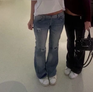 Lågmidjade bootcut jeans blå - Säljer ett par blå lågmidjade jeans med bootcut passform. Jeansen har slitna detaljer och hål vid knäna för en trendig look. Perfekta för dig som gillar en avslappnad och cool stil.