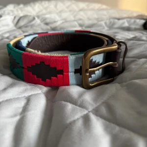 Pampeano bälte  - Säljer ett snyggt bälte från Pampeano i mörkbrunt skinn med färger. Väldigt fint skick. 100 cm