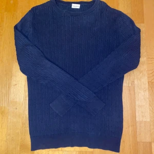 Marinblå stickad tröja John Henric - Säljer en marinblå stickad tröja från John Henric med klassiskt kabelstickat mönster. Tröjan har rund halsringning och långa ärmar, perfekt för lager-på-lager under kyliga dagar.