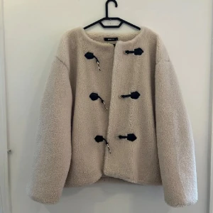 Beige teddyjacka från Gina Tricot - Supermjuk och fluffig beige teddyjacka från Gina Tricot med svarta detaljer och snygga snörningsspännen framtill. Som ny! Pris kan diskuteras!