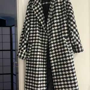 Svartvit rutig kappa med oversized passform - Säljer en svartvit kappa med klassiskt rutigt mönster och oversized passform. Jackan har bred krage, långa ärmar och är fodrad på insidan. Perfekt för dig som vill sticka ut med en trendig och tidlös look.