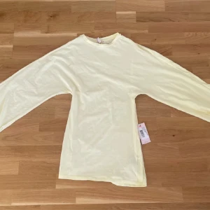 Ljusgul långärmad klänning - Enkel och stilren ljusgul långärmad klänning med rund halsringning. Klänningen har en rak passform och är tillverkad i ett mjukt bomullsmaterial som känns skönt mot huden. Perfekt att matcha med jeans eller kjol för en fräsch look.