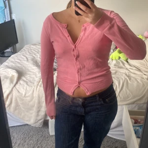 Rosa kofta från H&M med knappar - Söt rosa kofta från H&M med långa ärmar och knappar hela vägen framtill. Tröjan är i mjuk bomullsmix och har ribbade muddar vid ärmslut och nederkant. Perfekt att styla med jeans eller kjol för en chill look. 