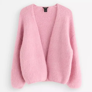 Rosa stickad kofta från LinDEX - Mysig rosa stickad kofta från LinDEX med oversized passform och långärmade ärmar. Koftan har en öppen front utan knappar och är tillverkad i ett fluffigt, mjukt material som känns extra skönt under kyliga dagar.