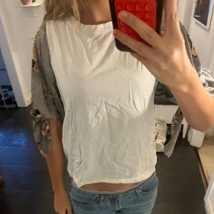 Vit blus med grå tigermönstrade ärmar - Unik blus med vit kropp i mjuk bomull och grå, flowiga ärmar med coolt tigermönster. Ärmarna har slits och knyt vid armbågen för extra edge. Perfekt för dig som vill sticka ut med djurprint och chill vibe.🍓