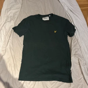 Mörkgrön t-shirt från Lyle & Scott - Snygg mörkgrön t-shirt från Lyle & Scott med klassisk rund hals och korta ärmar. På bröstet sitter den ikoniska gula fågeln broderad. Tillverkad i ekologisk bomull för skön känsla och stilren look. Helt ny saknar dock lapp
