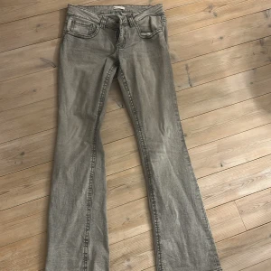 Grå bootcut jeans från Gina - Snygga grå jeans från Gina med bootcut-modell. Jeansen har klassiska fem fickor, bälteshällor och knäppning fram. Bakfickorna har lock och knappdetalj. Perfekt för dig som gillar en lite utsvängd siluett och cool tvätt.