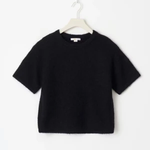 Svart stickad kortärmad tröja - En svart stickad tröja med korta ärmar och rund hals. Tröjan har en enkel och stilren design med lite boxig passform, perfekt att matcha med jeans eller kjol för en chill look.