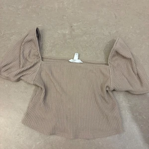 Beige ribbad offshoulder topp H&M - Säljer en beige ribbad topp från H&M i storlek M. Toppen har offshoulder-modell med puffiga korta ärmar och är tillverkad i ett mjukt, stretchigt material. Perfekt för en trendig och avslappnad look.