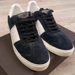 Valentino skor blår/vit - Snygga sneakers från Valentino Garavani i mörkblå mocka med vita skinnpaneler och coola nitar runt sulan. Klassisk rund tå, svarta snören och vit platt sula. Perfekta för dig som vill ha en lyxig och edgy look med exklusiva detaljer.