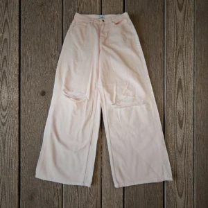 Ljusrosa wide jeans från Stay - Säljer ett par ljusrosa jeans från Stay med breda ben och slitna detaljer vid knäna. Byxorna har hög midja och klassisk femficksdesign. Perfekta för dig som gillar en avslappnad och trendig look.