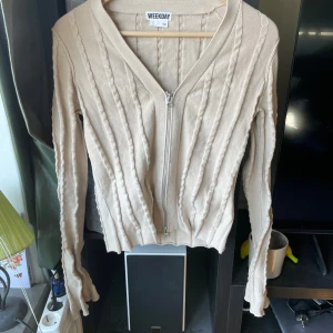 Beige kofta med dragkedja från Weekday - Säljer en beige kofta från Weekday i storlek S. Koftan är stickad med vertikala strukturränder, har v-ringning och hel dragkedja framtill. Långärmad och i mjukt material som känns skönt mot huden. Perfekt för lager-på-lager och snygg till jeans.