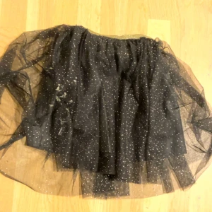 Svart glittrig kortkjol från KappAhl - Supersnygg svart kortkjol från KappAhl med glittriga prickar över hela tyget. Kjolen har flera lager tunn tyll som ger en fluffig och cool look. Perfekt för dig som vill sticka ut med lite extra glitter och volym.