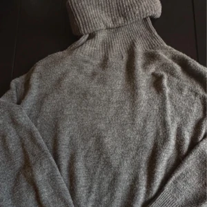 Grå polotröja i mjuk ullmix - Säljer en stilren grå polotröja med hög, ribbad krage och långa ärmar. Tröjan är i mjuk ullmix och har en klassisk, loose passform som är perfekt för kyliga dagar. Enkel att matcha med jeans eller kjol för en chill look.