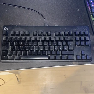 Logitech G Pro Mechanical Gaming Keyboard - Logitech G Pro mekaniskt gamingtangentbord med kompakt design och RGB-belysning. TKL-layout, dedikerade gaming- och ljusknappar. Synligt damm, men fullt fungerande. Perfekt för e-sport och gaming.