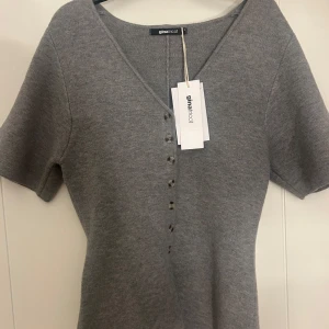 Grå kortärmad kofta från Gina Tricot - Superfin grå kofta från Gina Tricot med korta ärmar och v-ringning. Koftan har snygga knappar framtill och är stickad i mjukt material. Perfekt att slänga på sig över ett linne eller t-shirt för en chill look.