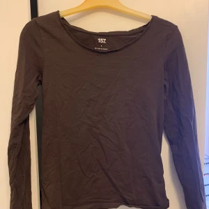 Brun långärmad topp från 157 - En enkel brun långärmad topp från 157 i storlek S. Tillverkad av mjuk bomull med lite stretch för skön passform. Rund halsringning och klassisk, rak modell som funkar till allt. Perfekt att styla med jeans eller kjol för en chill look.