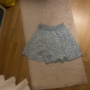 Blommig blå kortkjol från 157 - Supersöt blå kortkjol från 157 med vitt och svart blommönster. Kjolen har resår i midjan för en bekväm passform och är perfekt för varma dagar. Tunt och lätt material som ger en luftig känsla. Passar dig som gillar en feminin och avslappnad stil.