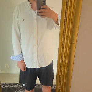 Vit skjorta från Polo Ralph Lauren XL - Vit långärmad skjorta från Polo Ralph Lauren i bomull i storlek XL/L. Klassisk passform med knappar framtill och broderad logga på bröstet. Manschetterna har blå- och vitrandigt tyg på insidan för en snygg kontrast. Pris kan diskuteras 