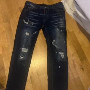 Disquared2 jeans - Säljer ett par mörkblå Dsquared2 Icon jeans i storlek 48. Jeansen har coola slitningar, färgstänk och patch med 'ICON' och 'FOREIGN' på baksidan. Klassisk femficksmodell med raka ben och snygga detaljer. Perfekt för dig som gillar streetstyle. ÄKTA kom gärna med frågor 💙