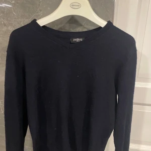 Mörkblå stickad tröja från Pre End - En stilren mörkblå stickad tröja från Pre End med v-ringad hals och lång ärm. Perfekt för lager-på-lager och enkel att matcha med jeans eller chinos. Klassisk passform och mjukt material som känns skönt mot huden.