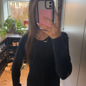 Marinblå stickad kofta med knappar - Mysig marin blå stickad kofta med knappar framtill. Tröjan har långärmad design och ett klassiskt kabelstickat mönster som ger en stilren och tidlös look. Perfekt att slänga på sig när det är kyligt ute.