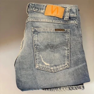 Blå nudie jeans med slitningar - Säljer nu dessa as feta blå jeans från Nudie Jeans med slitningar på benen och klassiska bakfickor med vågig söm. Jeansen har normal midja och är tillverkade i mjukt denimtyg. Riktigt feta slitningar och bra skick. Om frågor finns är det bara att kontakta direkt💫