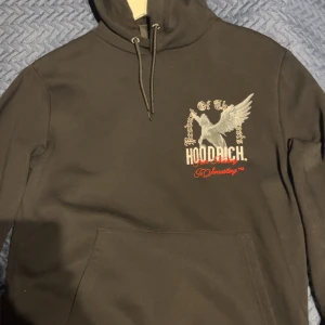 Svart hoodie från Hoodrich XS - Svart hoodie från Hoodrich i storlek XS med tryck av en bevingad häst och texten 'Product of the Streets' samt 'From Nothing To Something'. Hoodien har huva med snörning och stor ficka framtill. Snygga detaljer i vitt och rött på både fram- och baksidan.