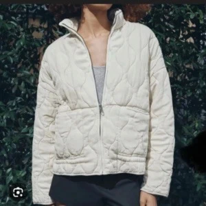 Quiltad vit jacka från Zara - Quiltad vit jacka från Zara med hög krage och dragkedja framtill. Jackan har två stora fickor och ett stilrent, oversized snitt. Perfekt för dig som gillar minimalistisk och clean stil. Materialet är mjukt och lätt, vilket gör den skön att bära under kyliga dagar.