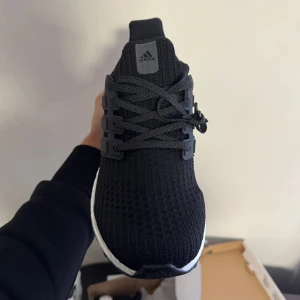 Adidas Ultraboost 1.0 svarta sneakers - Svarta Adidas Ultraboost sneakers med stickad ovandel och vit Boost-sula. Skorna har snörning, rund tå och diskreta detaljer i svart plast på sidorna. Perfekt för dig som gillar sportig och clean stil. Ultraboost-logga på hälen och BOOST-tryck på innersulan.