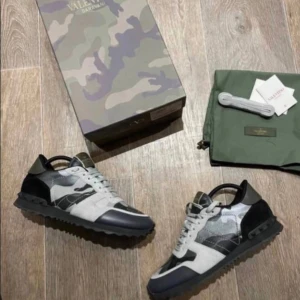 Valentino Rockrunners - Snygga Valentino Rockrunner sneakers med grå, svart och vita camo-detaljer. Skorna har en cool mix av skinn och mocka, samt svarta nitar på sulan. Perfekta för dig som vill sticka ut med exklusiva och trendiga sneakers. De är i storlek 42 och är i helt nytt skick med allt og. De säljs för 2199kr och priset kan diskuteras!