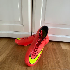Nike fotbollsskor i rött och gult - Säljer ett par Nike fotbollsskor i storlek 42. Skorna är röda med stora neongula Nike-loggor och svarta detaljer. De har snörning och dobbar i gult och rött för bra grepp på planen. Ovandelen är i syntetmaterial och insidan är svart och gul. Skorna är använda 1 gång! Då de inte passade mig.