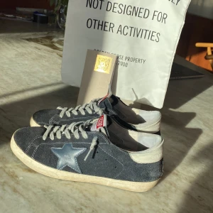 Golden Goose marinblå sneakers med röd lapp - Säljer ett par ovanliga golden goose i storlek 41 fast som sitter perfekt på mig med 42-42,5 i storlek. Box, dustbag och äkthetsbevis(golden goose passport) medföljer. Vid funderingar är det bara att skriva