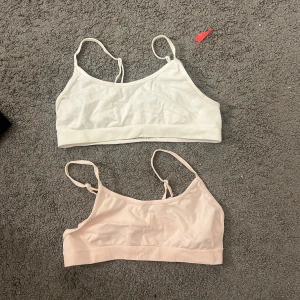 2-pack mjuka linne-toppar i bomull - Två mjuka linne-toppar från Cotton Italy, en i vit och en i ljusrosa. Båda har smala axelband och ärmlös design, tillverkade i skön bomull med stretchig ribbad kant nedtill. Perfekt för layering eller chill dagar. Säljes som 2-pack.