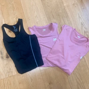 3-pack sporttoppar från Hummel - Säljer tre sporttoppar från Hummel: en svart linnetopp med brottarrygg och reflexdetalj, en rosa croppad ärmlös topp och en rosa kortärmad topp. Alla har Hummel-logga på bröstet och är i mjukt, stretchigt material som passar perfekt till träning.