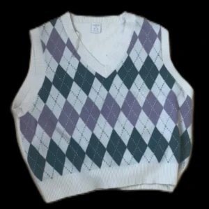 Rutig stickad väst med v-ringning - Snygg stickad väst med klassiskt rutig argyle-mönster i vitt, lila och mörkgrönt. Västen har v-ringad hals och ribbade kanter. Perfekt för lager-på-lager och ger en preppy vibe.