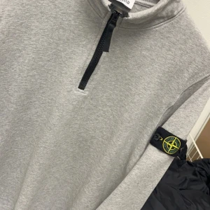 Grå half zip tröja från Stone Island - Snygg grå långärmad tröja från Stone Island med svart half zip-dragkedja och klassisk logga på ärmen. Storlek 14-16 och passar 155-170Perfekt för dig som gillar stilrena och sportiga plagg. Mjuk bomullskänsla och relaxed fit.