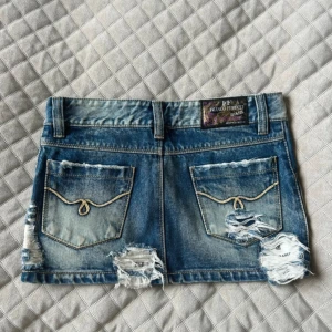 Blå jeanskjol - Snygg blå jeanskjol från Franco Ferucci med slitna detaljer och råa kanter. Kjolen har klassiska fickor både fram och bak, bälteshällor och coola slitningar som ger en trendig look. Perfekt för dig som gillar streetstyle och denim.