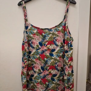Blommig linnetopp från myWear Woman - Säljer en färgglad linnetopp från myWear Woman i storlek L. Toppen har ett blommigt mönster med rosa, röda, blå och gröna toner. Den är ärmlös med smala axelband och har en mjuk, lätt bomullskänsla. Perfekt för dig som gillar somriga vibes och mycket färg!