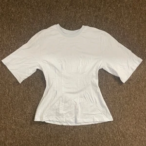 Ljusblå t-shirt från Stories XS - Snygg ljusblå t-shirt från Stories i storlek XS. Modellen har en figurnära passform med korta ärmar och rund halsringning. Tillverkad i mjuk bomull som känns skön mot huden. Perfekt för dig som gillar enkel och clean stil.