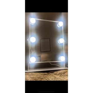 Sminkspegel med LED-belysning - Elegant sminkspegel med 8 starka LED-lampor för optimal belysning. Perfekt för makeup och styling. Vit ram och stabil fot. Spegeln är i mycket fint skick utan synliga repor eller skador. Touch-knapp för enkel av/på-funktion. Finns olika lägen för hur stark belysningen ska vara, du kan enkelt anpassa styrkan till ditt önskemål. Snygg och praktisk detalj till sminkbordet.                                                  34x30 cm. (Med foten).