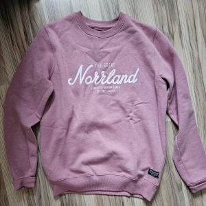 Rosa sweatshirt från SQRTN, S - Rosa sweatshirt från SQRTN med vit text 'The Great Norrland' framtill. Tröjan har rund hals, ribbade muddar och mjuk insida. Perfekt för dig som gillar streetwear med norrländsk vibe. Lite nopprig, men går o ta bort. 