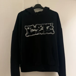 Svart hoodie Cease 2 Exist med tryck - Svart hoodie från Cease 2 Exist med stort grafiskt tryck fram och bak, samt detaljer på huvan. Oversized passform och slitna detaljer på ärmen.