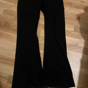 Svarta bootcut kostymbyxor Gina Tricot - Snygga svarta kostymbyxor från Gina Tricot i bootcut-modell. Byxorna har hög midja, klassisk dragkedja och hyska-knäppning fram. Materialet är mjukt och har en lätt stretch för skön passform. Använd några gånger.