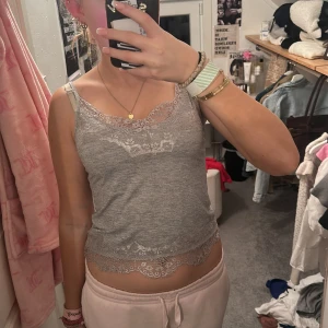 Grå linnetopp med spets från BikBok - Supersöt grå linnetopp från BikBok med tunna axelband och fina spetsdetaljer både upptill och nedtill. Toppen är figurnära och har en mjuk känsla, perfekt att styla med jeans eller kjol. Enkel men ändå extra med spetsen!