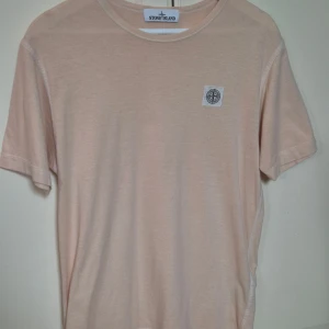  Stone Island t-shirt S - Säljer en stilren ljusbeige t-shirt från Stone Island med klassisk rund hals och liten logopatch på bröstet. T-shirten är i mjuk bomull och har en clean look som passar perfekt till jeans eller shorts. I mycket gott skick.