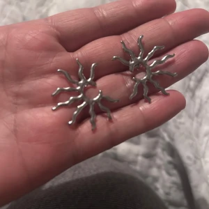 Solformade örhängen i silver - örhängen i form av en sol med vågiga strålar, tillverkade i stål blankt silverfärgat material. De har en cool  design som sticker ut och passar perfekt om du vill ha något annorlunda. Säljs som ett par.
