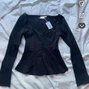 Svart peplumtop med lång ärm XXS - Säljer en svart peplumtop från NA-KD i storlek XXS. Toppen har lång ärm, fyrkantig halsringning och figurnära passform med utsvängd nederdel. Materialet är mjukt och stretchigt, perfekt för att ge en snygg siluett. Stilren och enkel att matcha med jeans eller kjol.