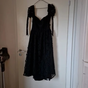 Svart blommig långklänning - Svart klänning som går ner till ungefär knäna på mig ( 168 cm lång ) med broderade blommor och spets/mesh. Den knyts vid ryggen och typ halva delen av ryggen är öppen. Den knyts även vid armarna. Använd bara en gång och är i väldigt bra skick förutom få lösa trådar. Katt finns i hemmet. Köpt på ASOS