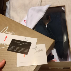 Mörkblå sneakers från Christian Louboutin - Exklusiva mörkblå sneakers från Christian Louboutin med ikonisk röd sula och snygg snörning. Skorna har en stilren design med rund tå och platt sula, tillverkade i skinn för en lyxig känsla. Perfekt för dig som vill sticka ut med ett statement-märke.